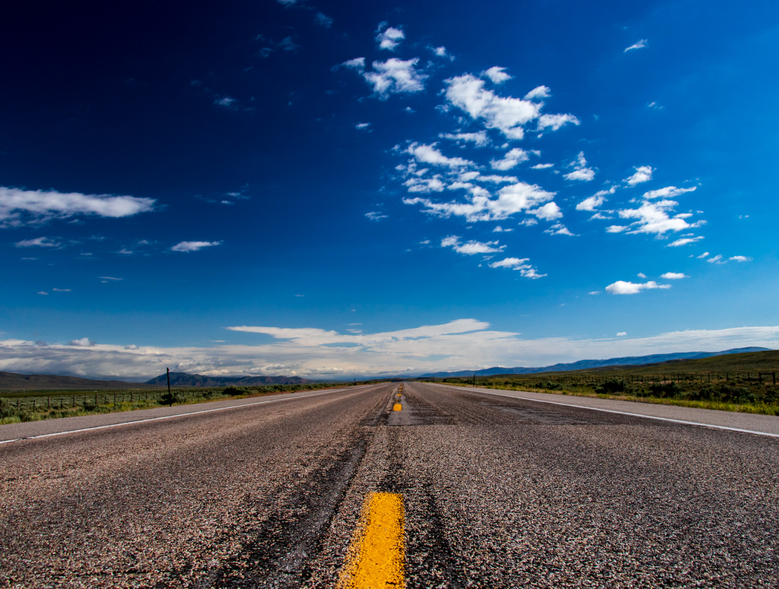 Two-lane highway stretching to the horizon through high desert under a deep blue sky
