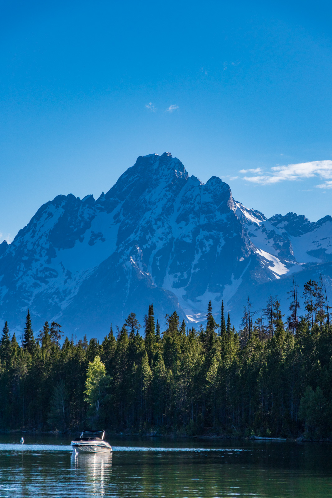 Motorboat on a mountain lake with snow-capped Grand Teton peak rising behind a forested shoreline